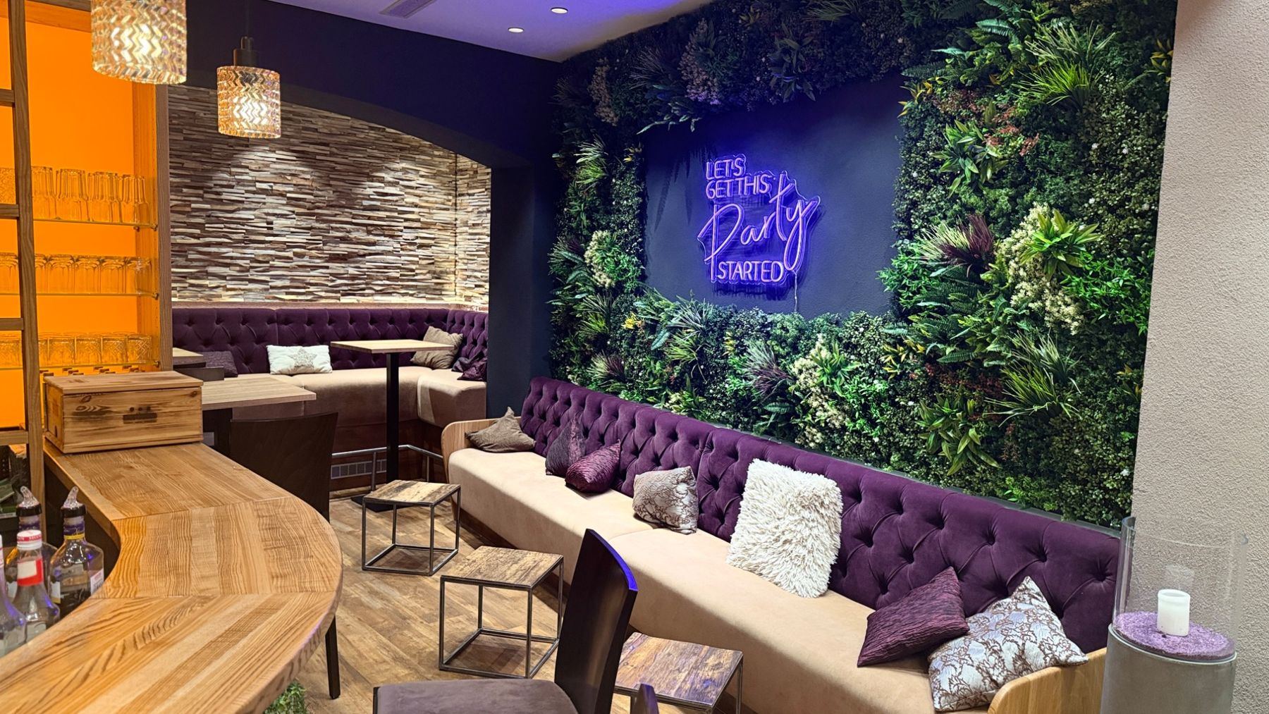 Lounge mit Sofas, Pflanzenwand und Neonschrift an der Bar